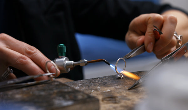 Soudure d'une bague à l’aide d’un chalumeau et d’une pince en atelier de joaillerie.