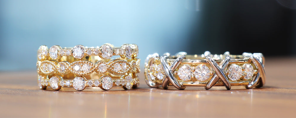 Ensemble de bagues créées sur mesure, l’une pour femme et l’autre pour homme. La bague femme est composée de trois anneaux empilés en or jaune, sertis de diamants ronds et marquises en serti clos et pavé, dans un design riche et étincelant. La bague homme, plus sobre mais audacieuse, présente une ligne de diamants sertis en rail, encadrés de croisés en or blanc formant un motif “X” sculptural sur le dessus du corps de bague.