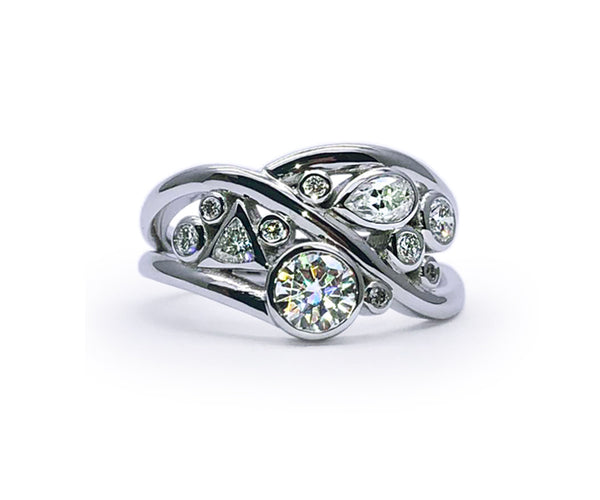 Création sur mesure en or blanc au design organique et enveloppant. Le corps de bague aux lignes croisées crée un mouvement fluide, mettant en valeur un mélange de diamants de formes variées — ronde, poire et triangle — en sertis clos.